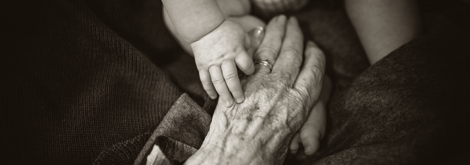 Older person's hand holding the hand and foot of a baby.