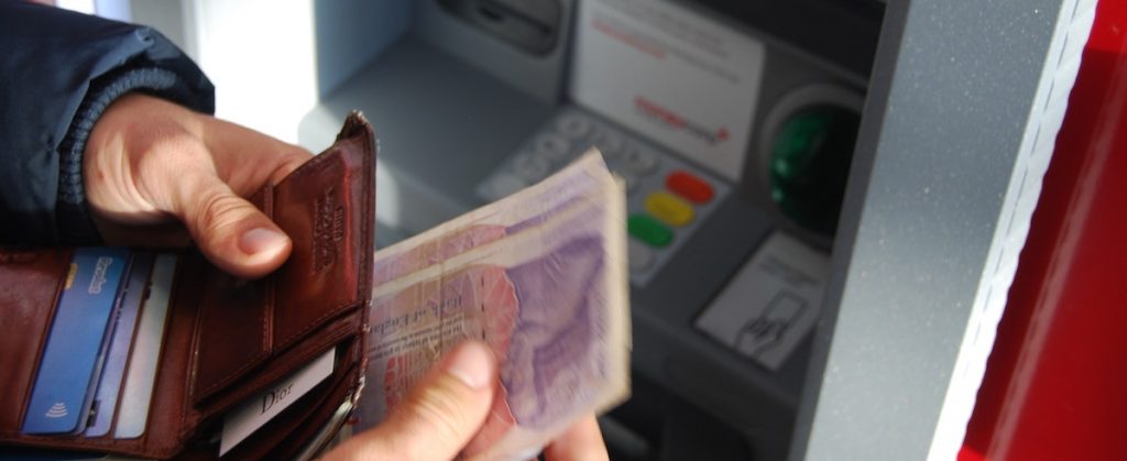 Man with wallet and a number of bills near an ATM.