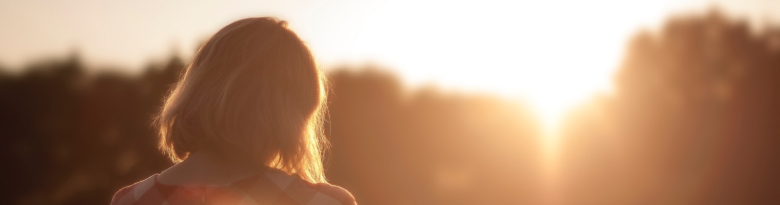 Woman contemplating if she should spend less or save more while looking at treeline and sunset.