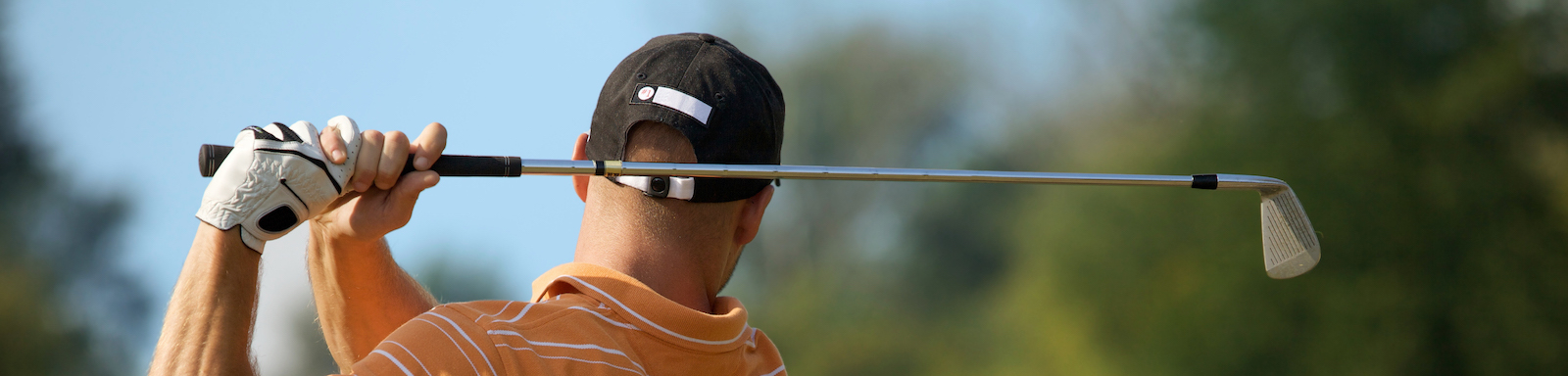 Young man swinging golf club, rear view